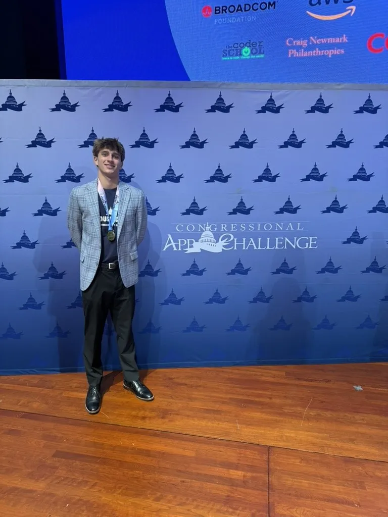 Maclane Zich wearing his winner's medal in front of the Congressional App Challenge backdrop