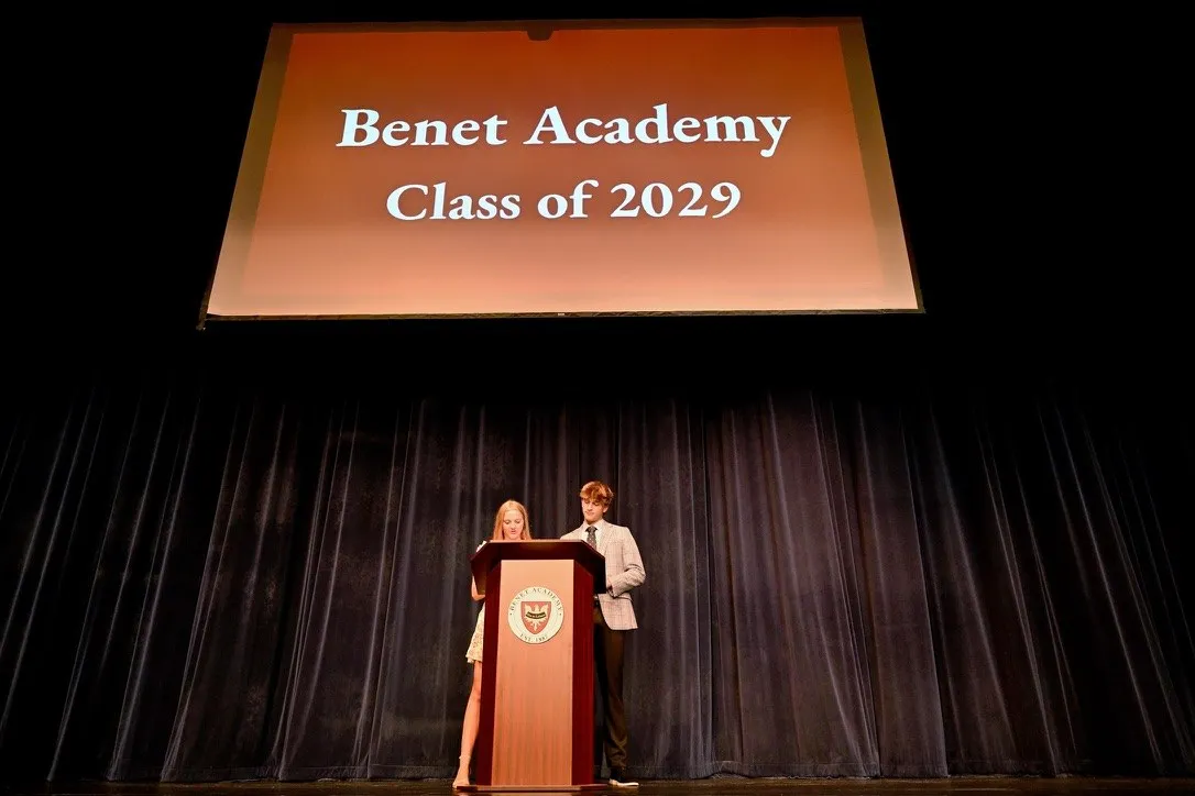 Maclane Zich co-emceeing at the Benet Academy podium beneath a Class of 2029 slide