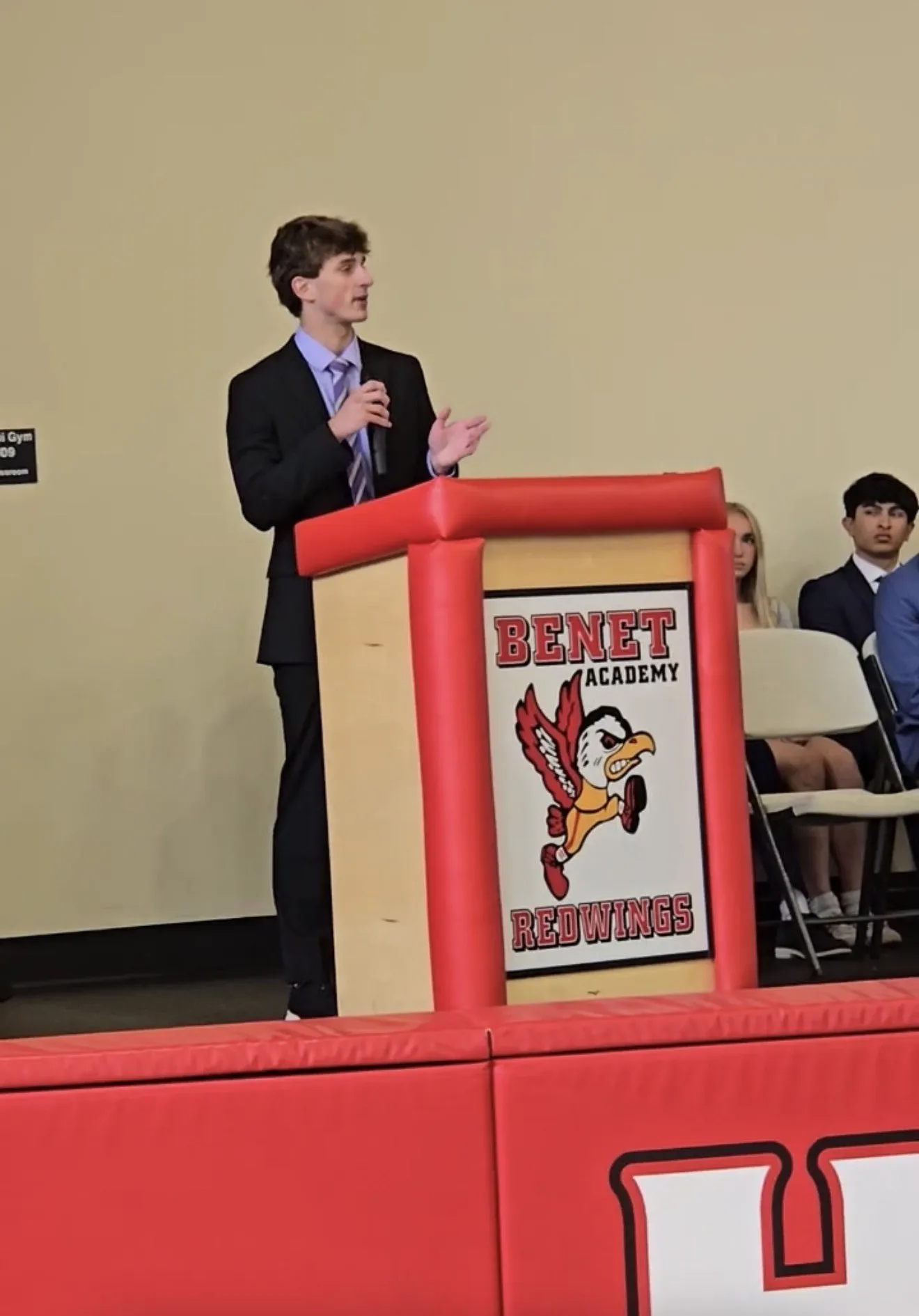 Maclane Zich speaking into a microphone at the Benet Academy Redwings podium